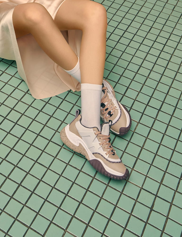 A pair of mesh chunky sneakers in nude pictured against green square tiles – sitting.