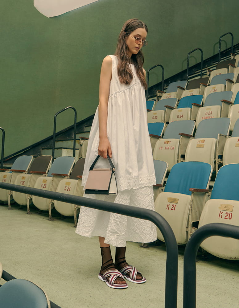 A model in grosgrain slide sandals, a sculptural bag and round tinted sunglasses.