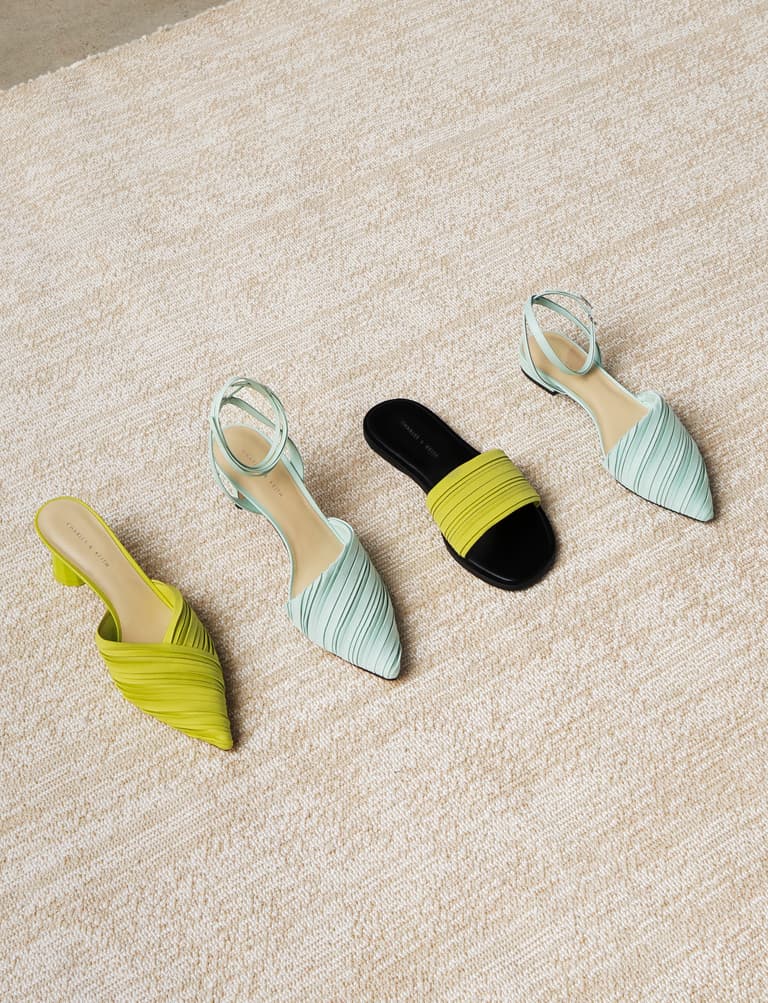 A flat lay featuring pleated pointed-toe mules, ankle tie stiletto pumps, slide sandals, and ankle strap flat pumps in mint green and neon yellow