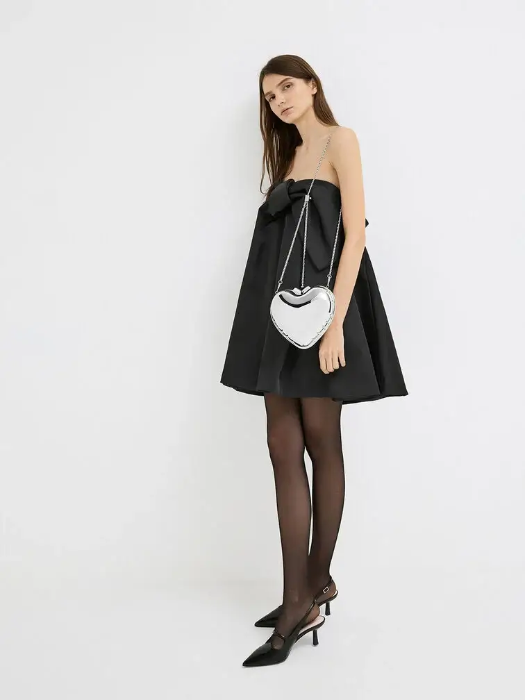 Metallic heart-shaped clutch with chain strap, styled with a black mini dress for holiday parties.