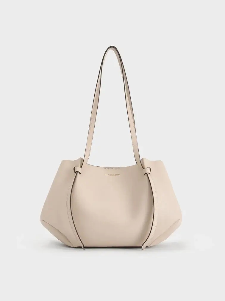 The Calla tote bag in oat with the side magnetic clasps folded in to create a geometric-like shape 